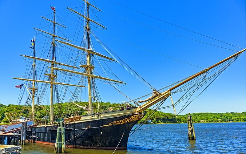 A historic tall ship docked on a calm body of water against a clear blue sky.
