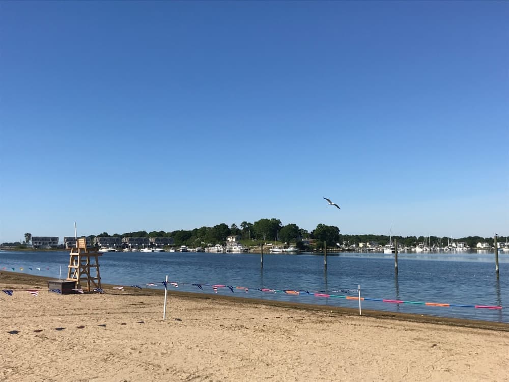 A sandy beach with a lifeguard stand overlooking a calm bay under a clear blue sky.