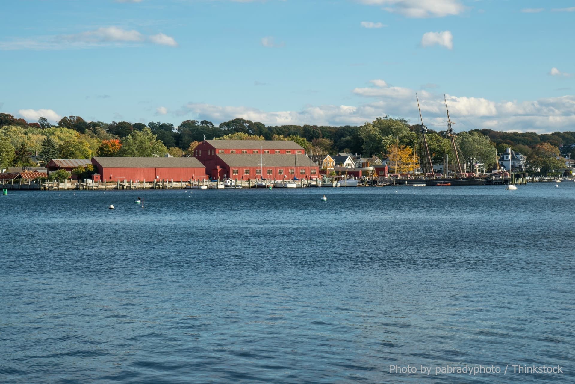 A tranquil harbor scene featuring a red building and a sailboat, surrounded by autumn foliage.