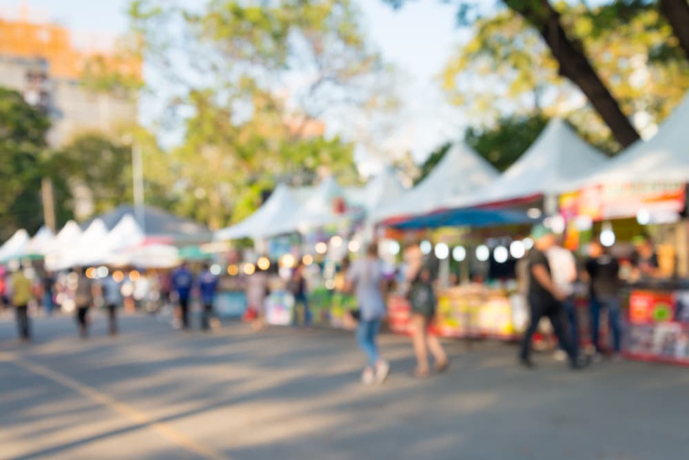 A blurred view of a lively outdoor market with food stalls and visitors.