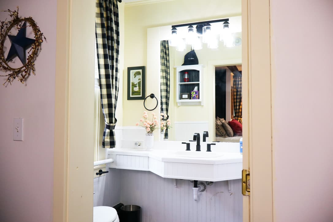 A view into a cozy bathroom featuring a white sink, black fixtures, plaid curtains, and decorative elements.