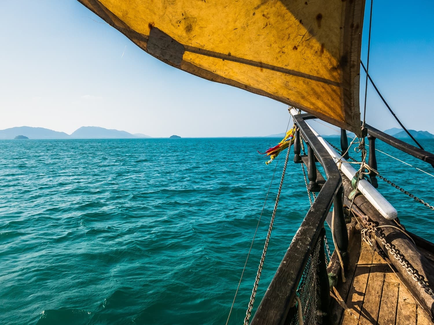 View from a boat with a yellow sail over turquoise water and distant islands.