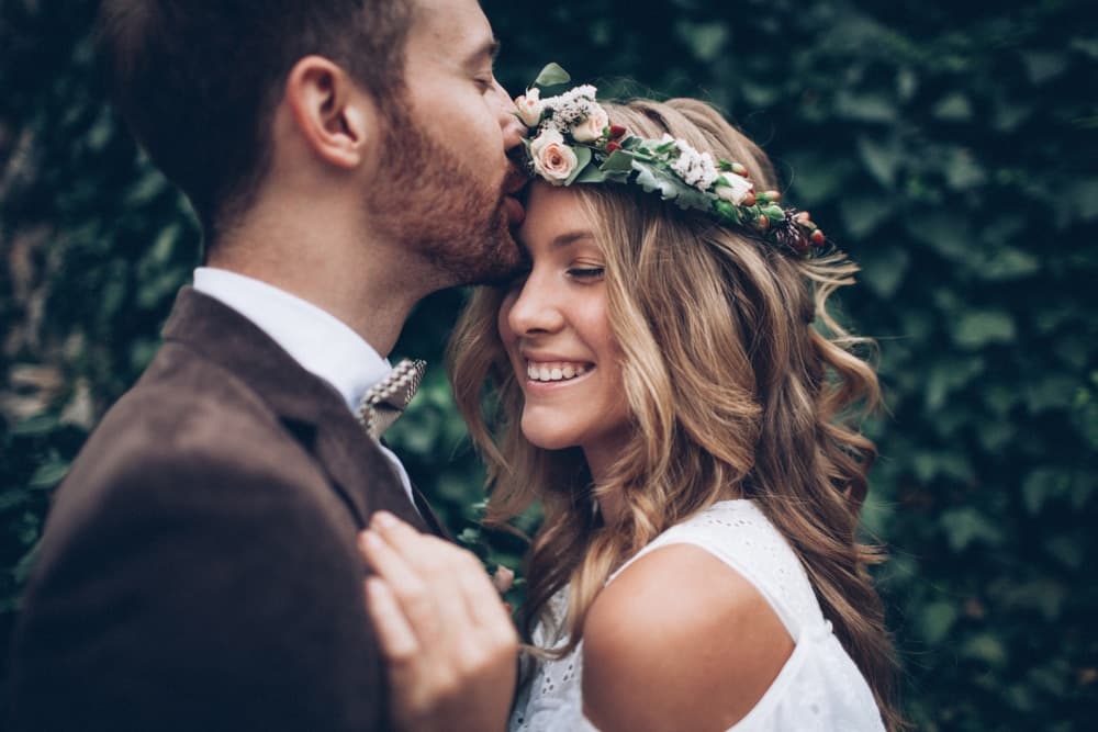 A couple embraces tenderly, with the woman wearing a floral crown and smiling joyfully.