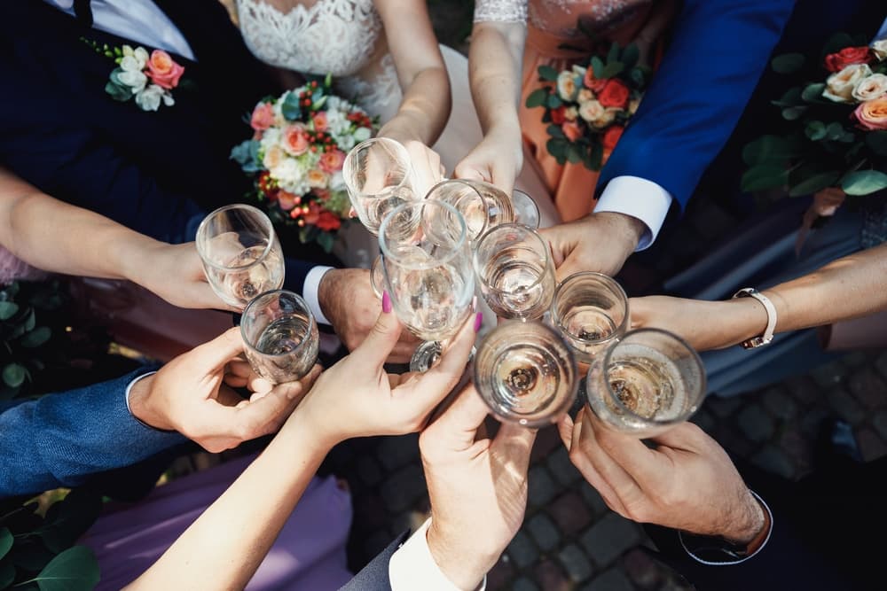 A group of hands raises glasses in a celebratory toast at a wedding.