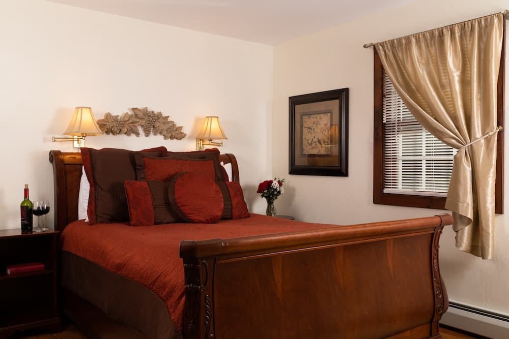 A cozy bedroom featuring a wooden sleigh bed with red and brown accents, two bedside lamps, and a framed artwork on the wall.