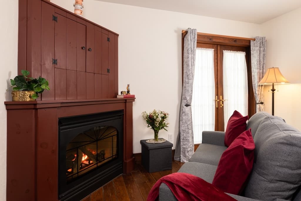 Cozy living room featuring a fireplace, a gray sofa with red cushions, and light curtains around French doors.