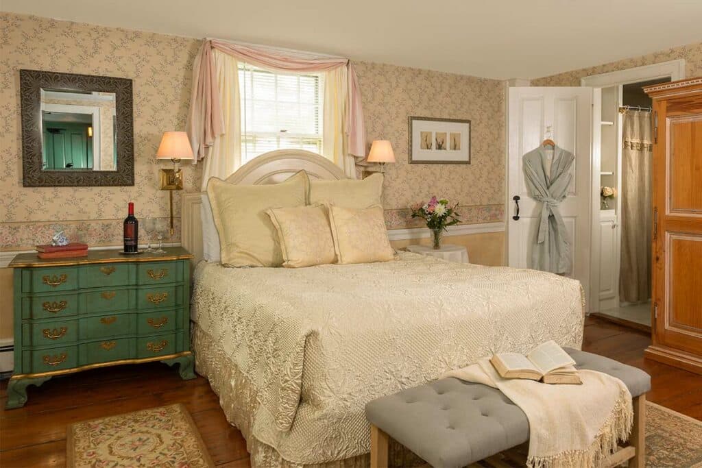 Cozy bedroom featuring a large bed with decorative pillows, a green nightstand, and a robe hanging by a door.