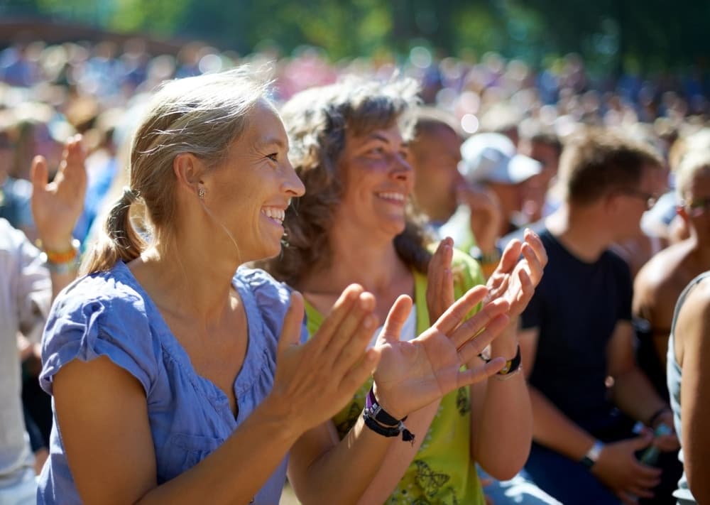Two women are smiling and applauding in a crowded outdoor setting.