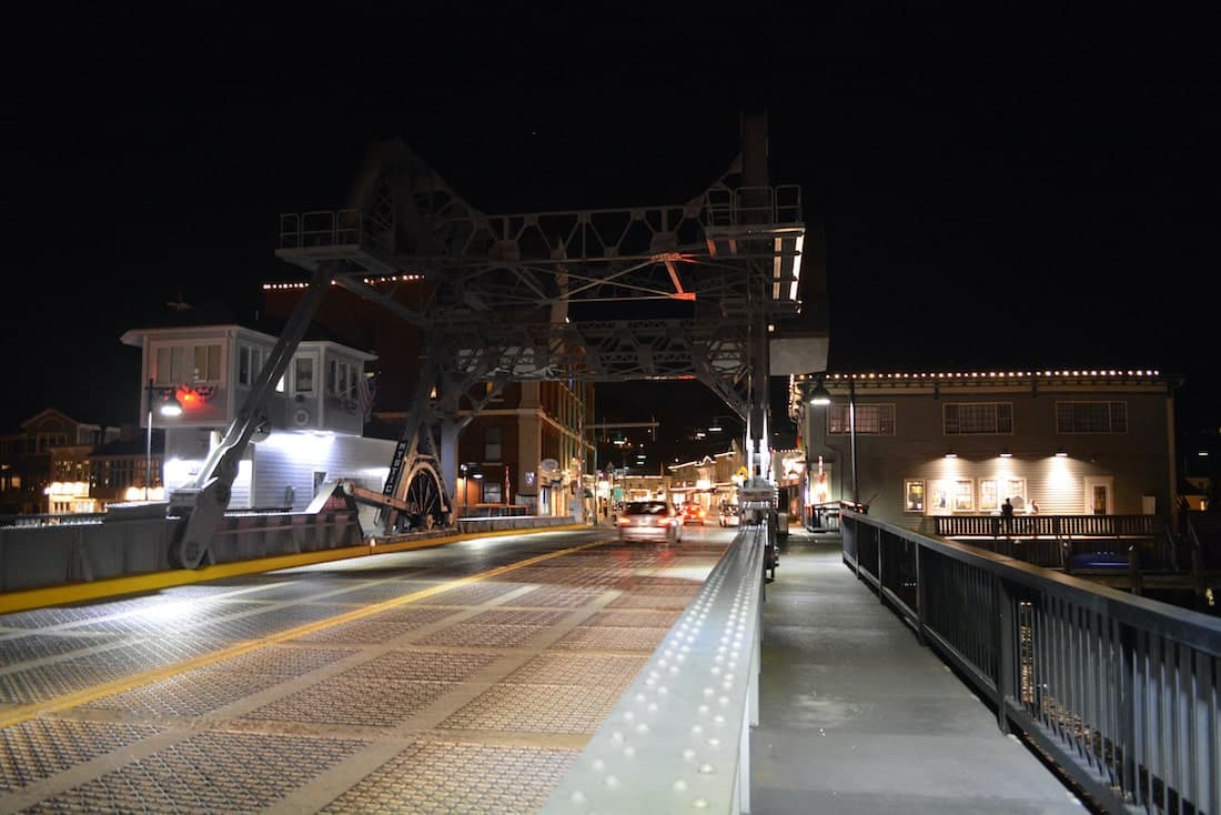 A drawbridge is raised at night, illuminating the surrounding buildings and streets.