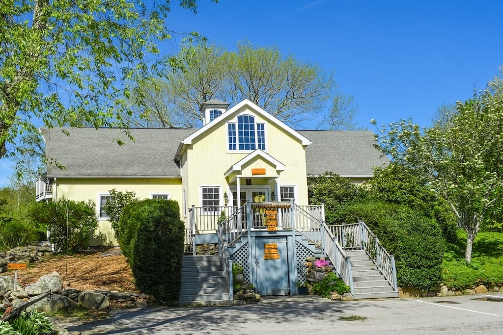 A yellow house with a gabled roof, surrounded by greenery and a clear blue sky.