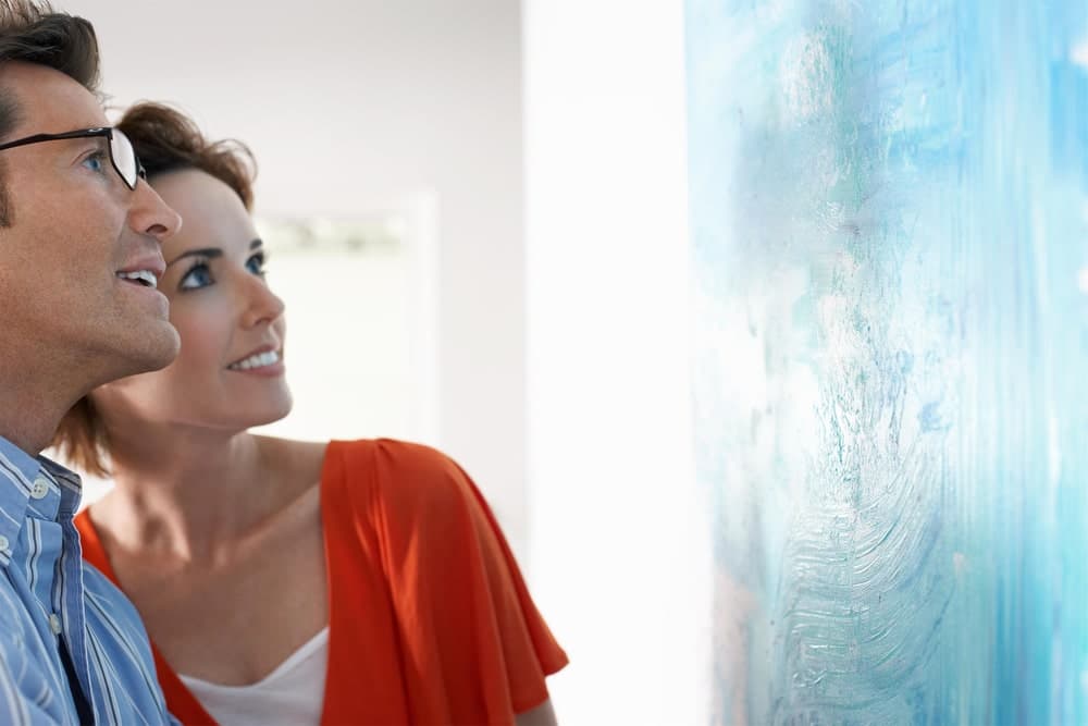 A man and woman admire a blue abstract painting in a modern gallery.