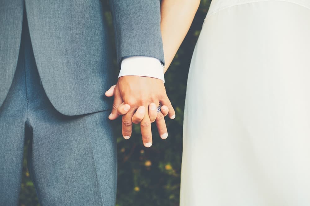 A close-up of a man and woman holding hands, showcasing their wedding rings.