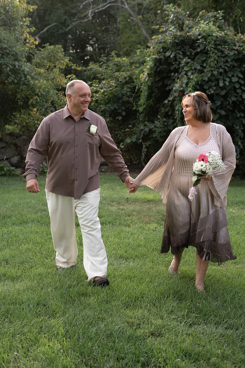 A couple joyfully walks hand in hand through a lush garden, enjoying a moment together.