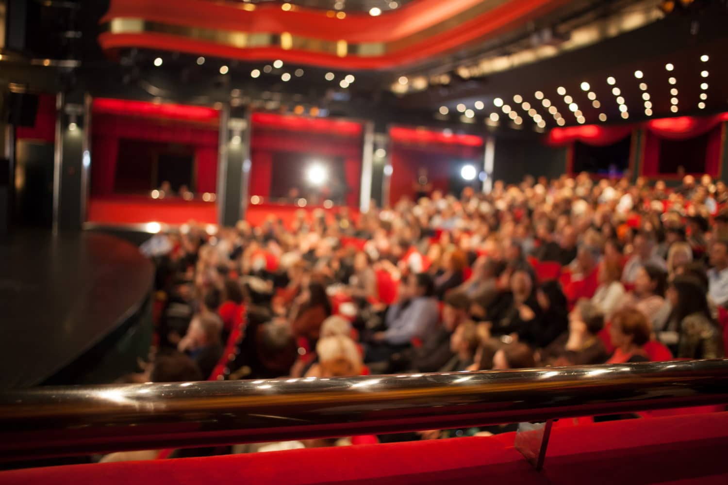 A blurred view of a large audience seated in a theater with red accents.