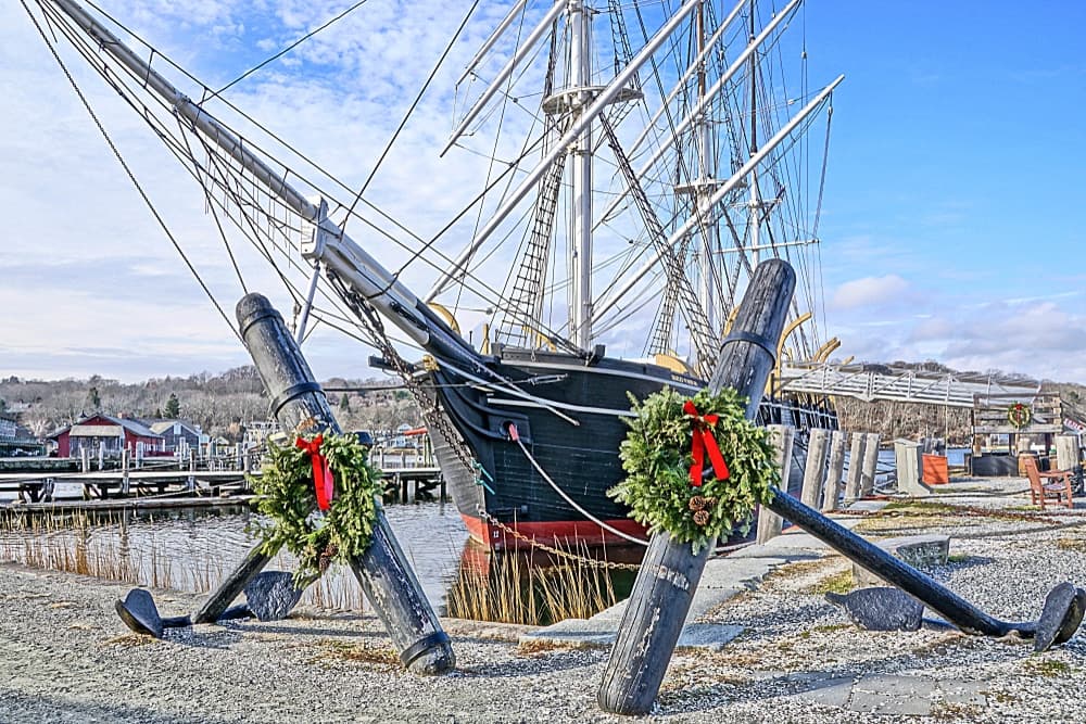 A historic ship adorned with festive wreaths is docked at a waterfront.