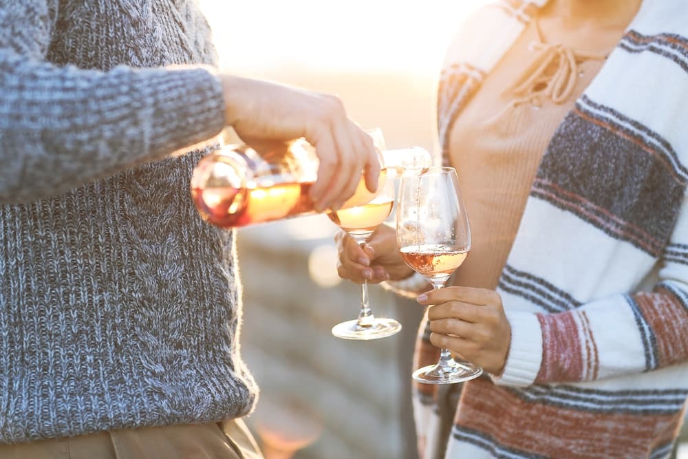A person pours rosé into a glass held by another person, both enjoying a sunny outdoor setting.