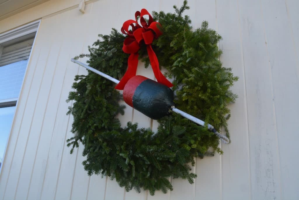 A festive wreath decorated with a red ribbon and a fishing buoy.