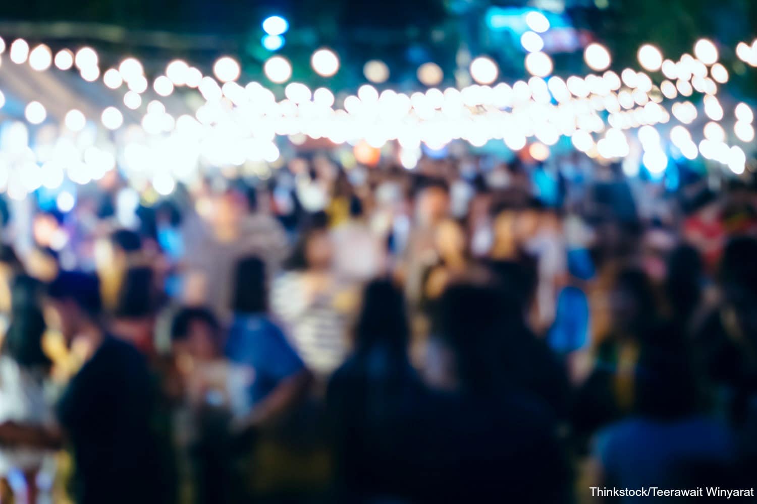 A blurred scene of a crowded event illuminated by string lights.