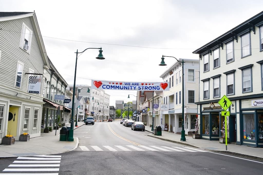 A quiet town street features a banner reading "We Are Community Strong."