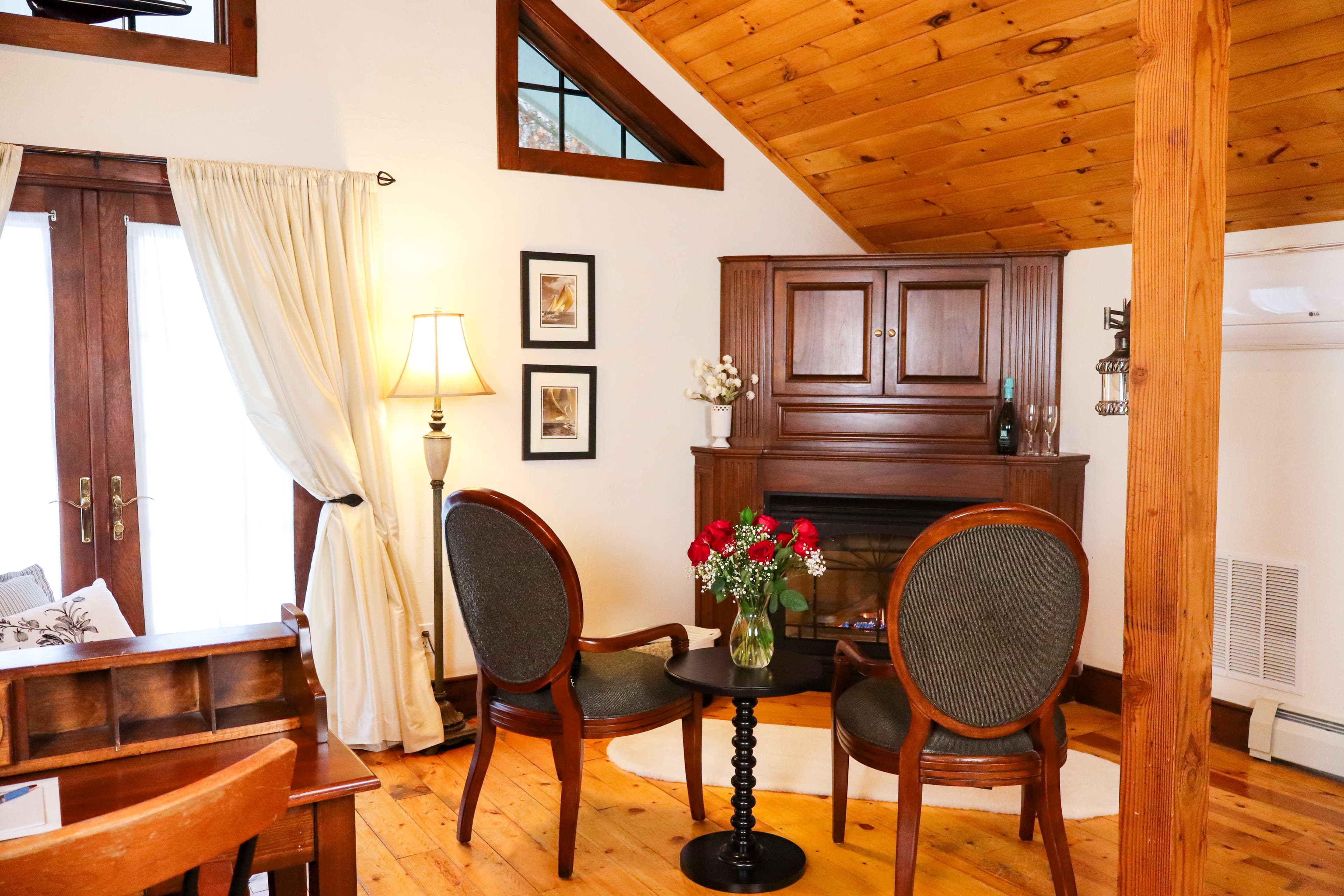 Cozy living space featuring two chairs, a table with flowers, and a wooden cabinet under a sloped ceiling.