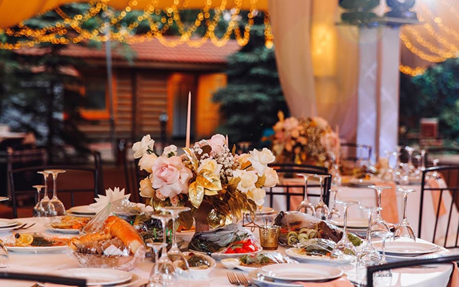 A beautifully set dining table adorned with floral centerpieces and an array of dishes, under twinkling lights.