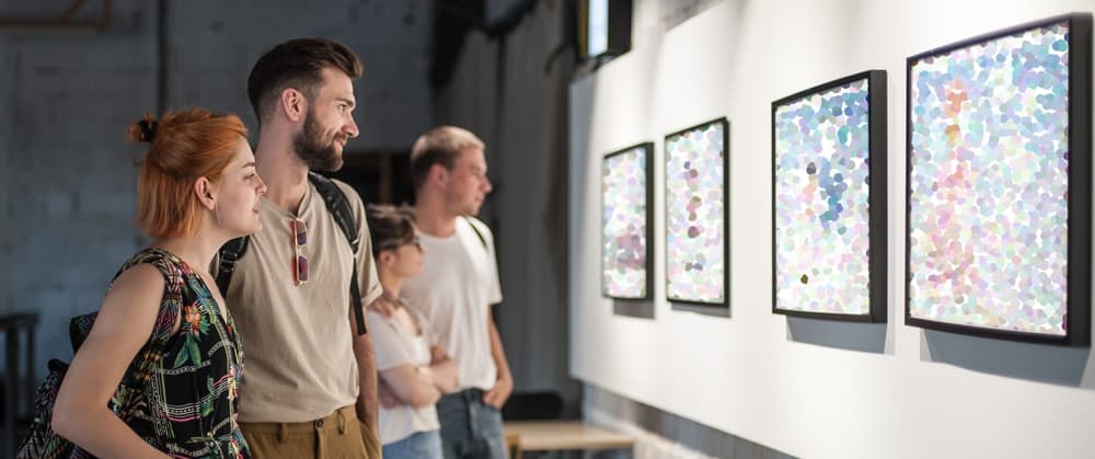 Four people are admiring colorful abstract artworks displayed on a gallery wall.