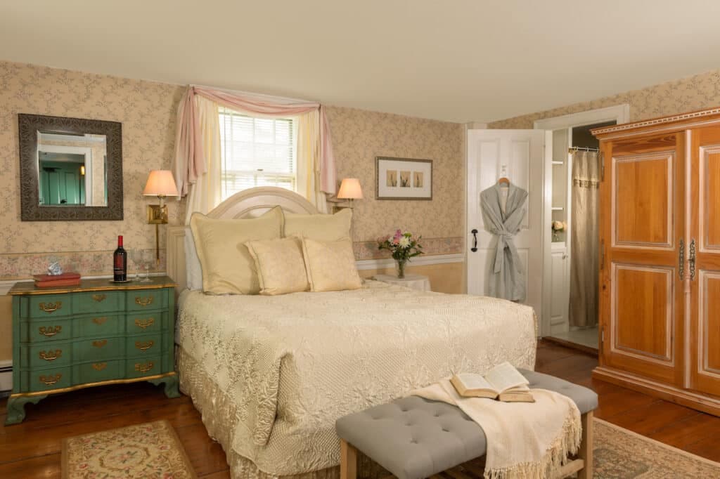A cozy bedroom featuring a large bed, decorative accents, a green dresser, and a robe hanging near a closet.