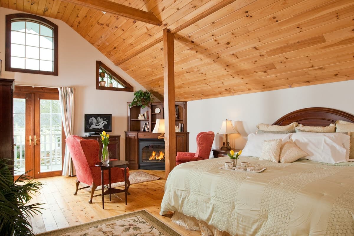 Cozy bedroom with wooden ceilings, a large bed, and a seating area by a fireplace.