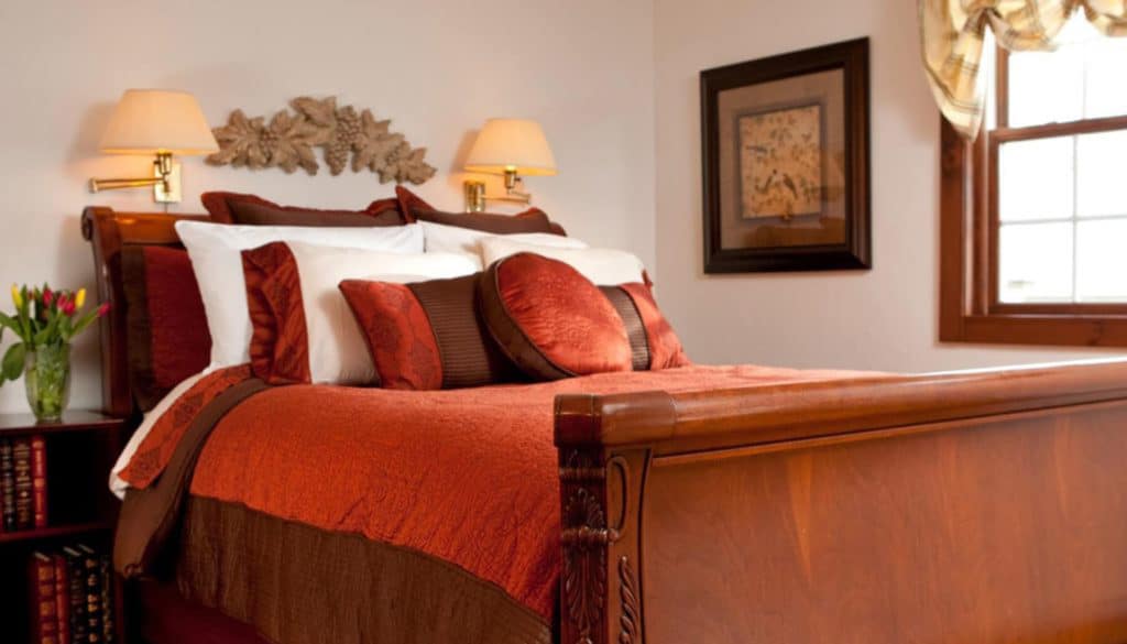 A cozy bedroom featuring a wooden bed with red and brown bedding and decorative pillows.