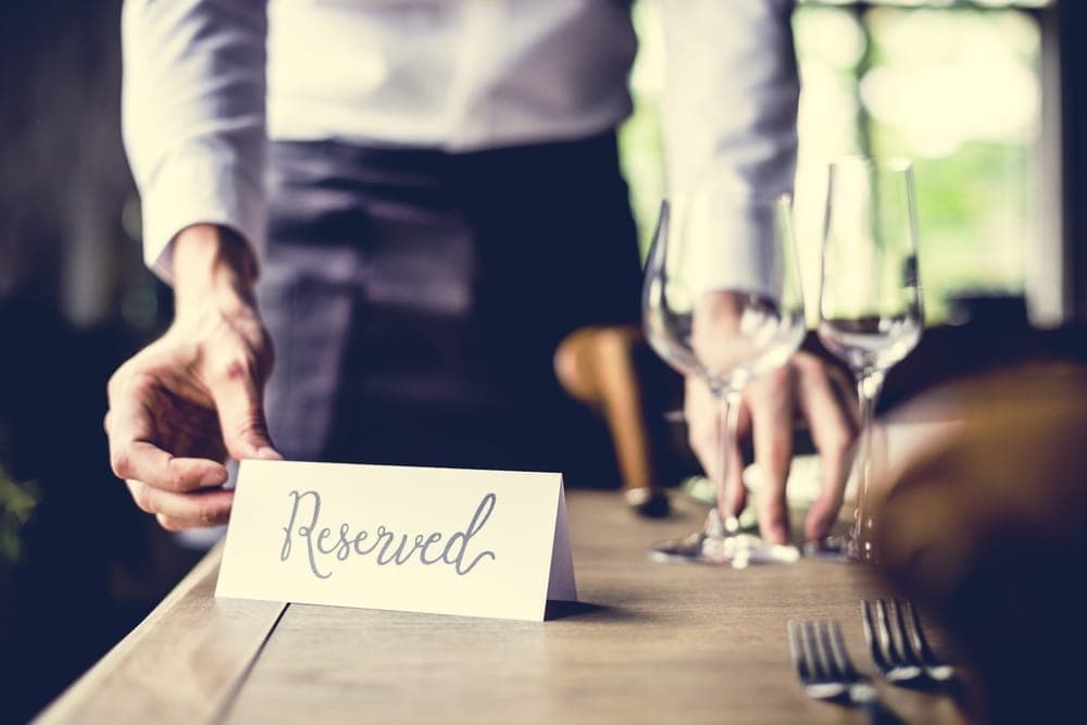 A waiter places a "Reserved" sign on a table set with glasses and cutlery.