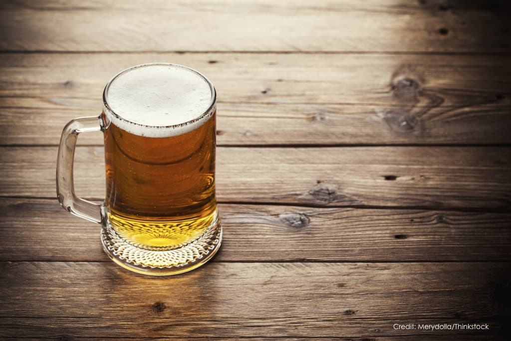 A frosty mug of beer sits on a rustic wooden table.