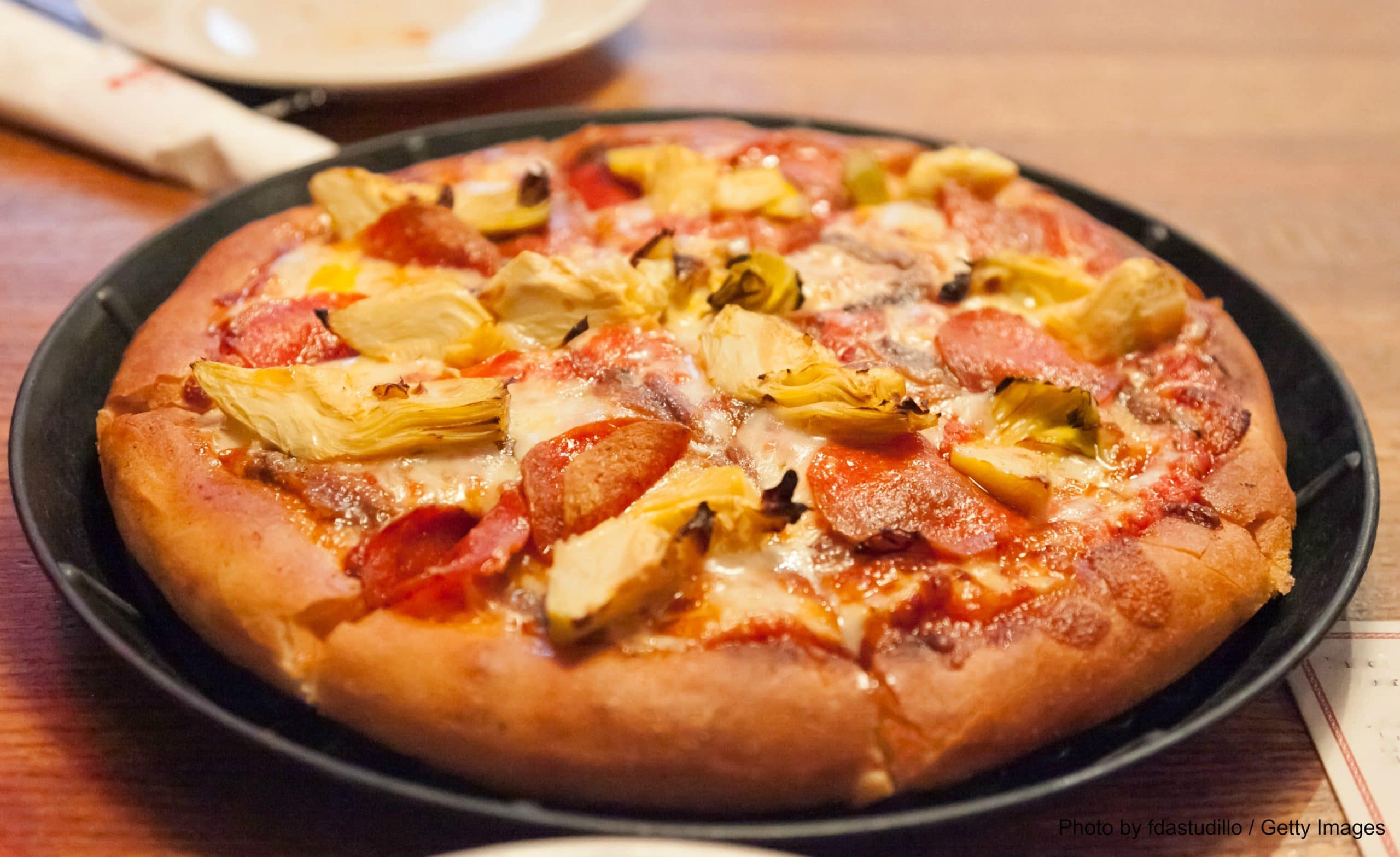 A pizza topped with pepperoni, artichoke hearts, and melted cheese on a dark plate.