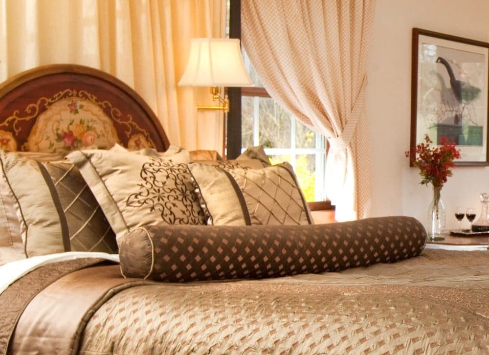 A stylish bedroom featuring a large bed adorned with decorative pillows and a floral headboard, complemented by soft drapes and elegant decor.