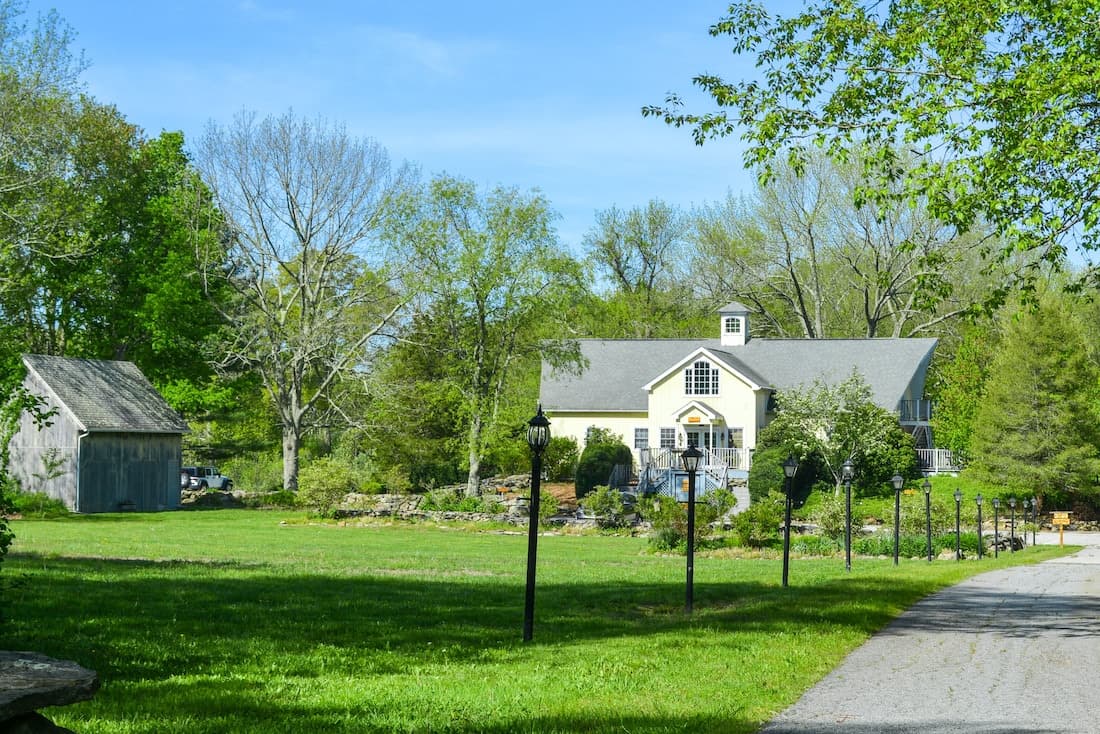 A charming house surrounded by lush greenery and trees, with a gravel path leading to it.