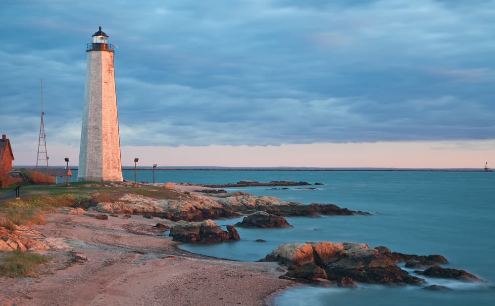 A tall lighthouse stands on a rocky shore under a cloudy sky.