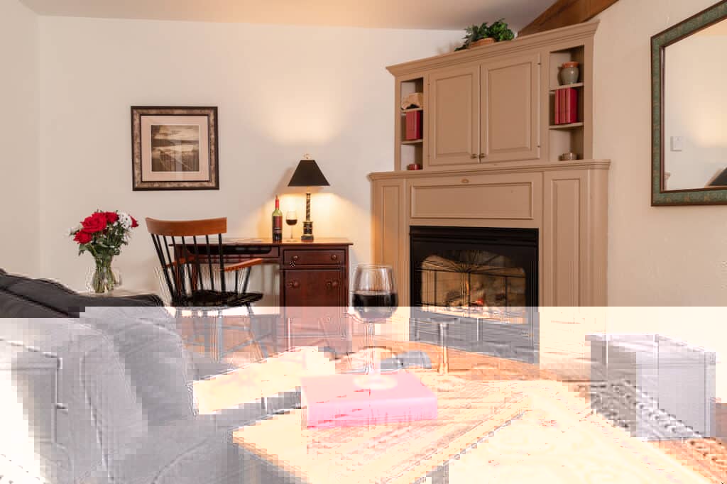 A cozy living room featuring a fireplace, a chair, a table with a wine glass, and a vase of flowers.