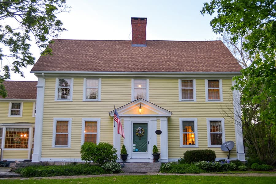 A large yellow house with white trims and an American flag in front.