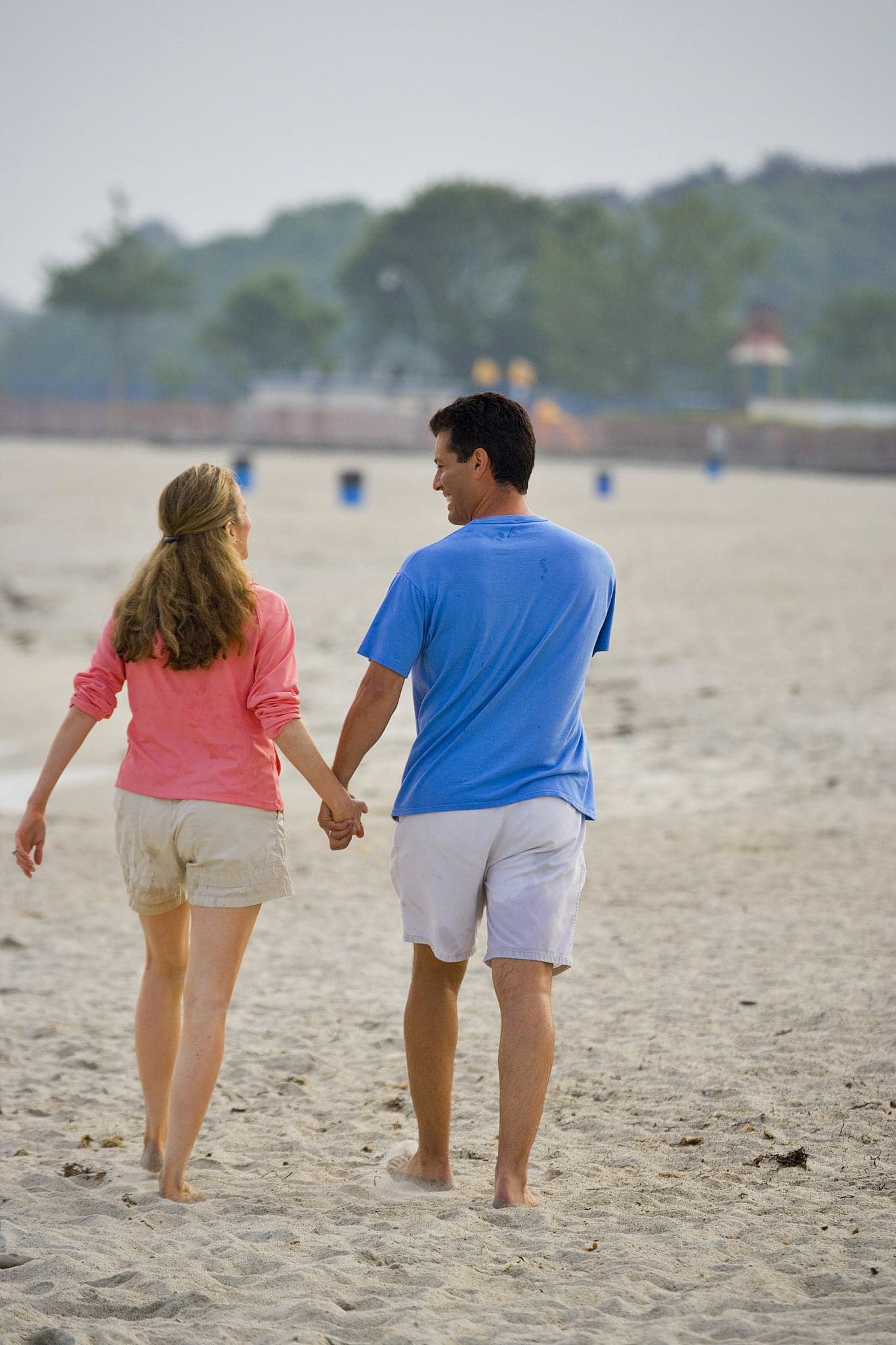 A couple strolls hand-in-hand along a sandy beach.