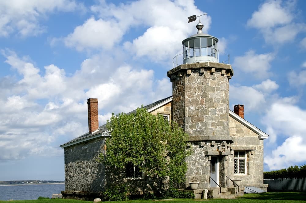 A stone lighthouse surrounded by green grass and a blue sky with clouds.