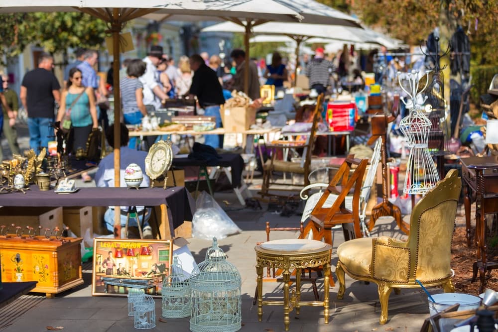 A bustling outdoor market filled with vintage items and furniture under sun umbrellas.