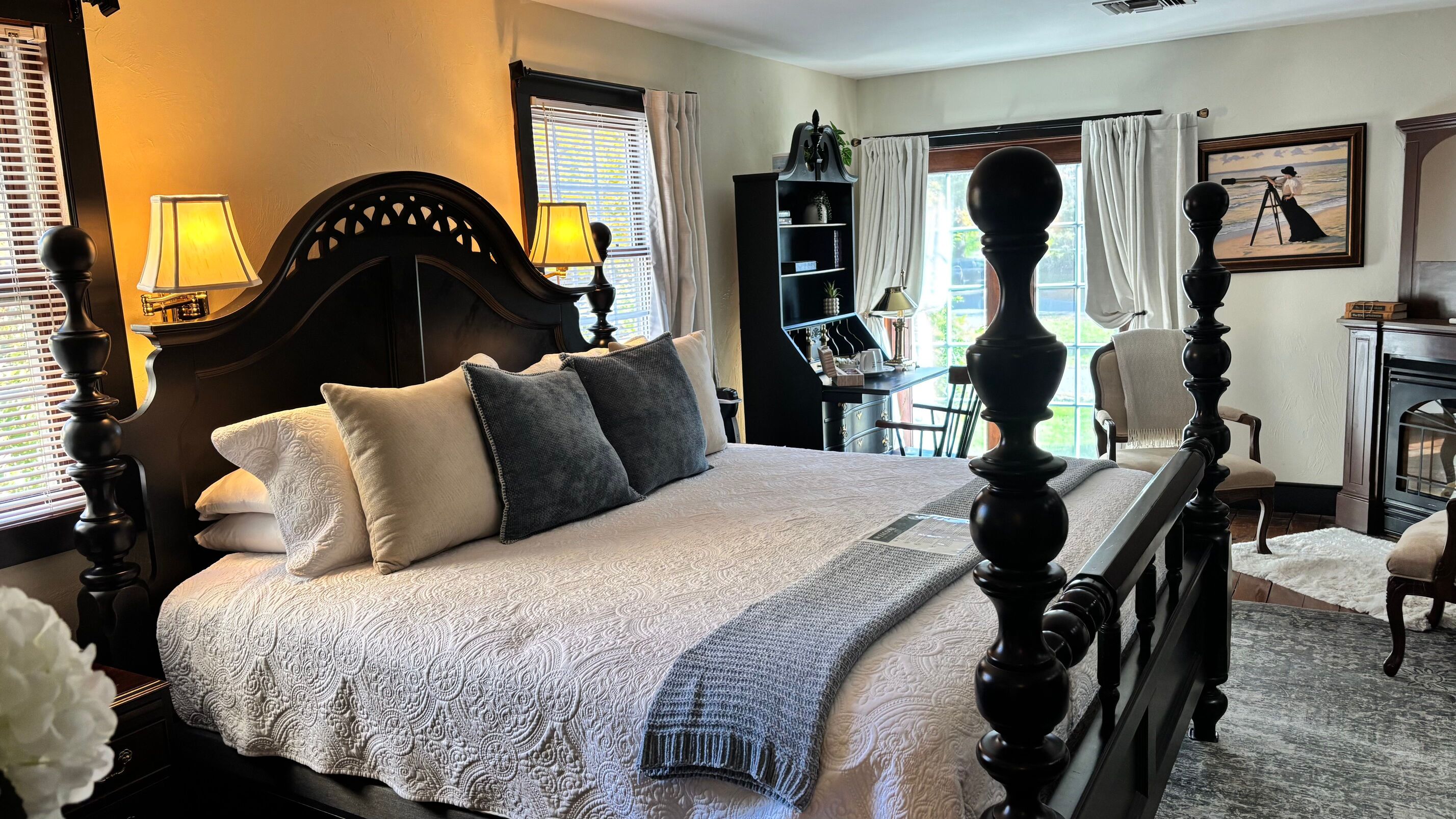 A cozy bedroom featuring a dark wooden bed, decorative pillows, a desk area, and warm lighting.
