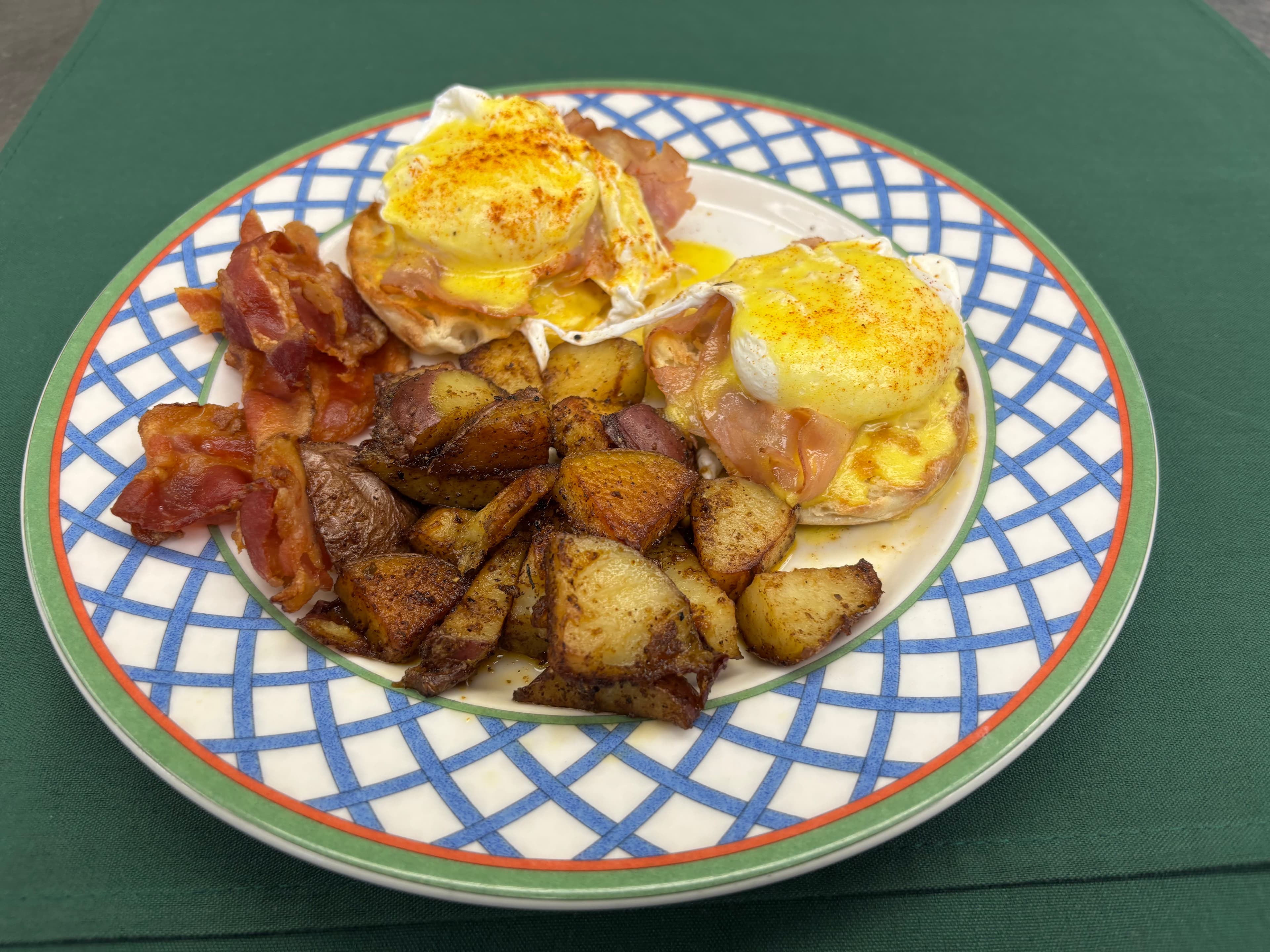 A plate of eggs Benedict with bacon and seasoned roasted potatoes.