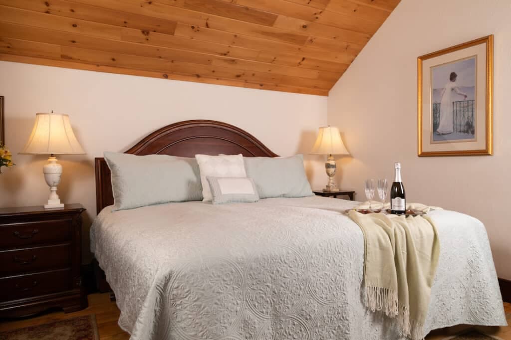 Cozy bedroom featuring a large bed with soft linens, bedside tables with lamps, and a bottle of champagne with glasses.