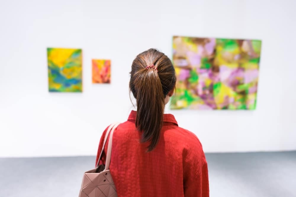 A woman in a red jacket gazes at colorful abstract artworks in a gallery.