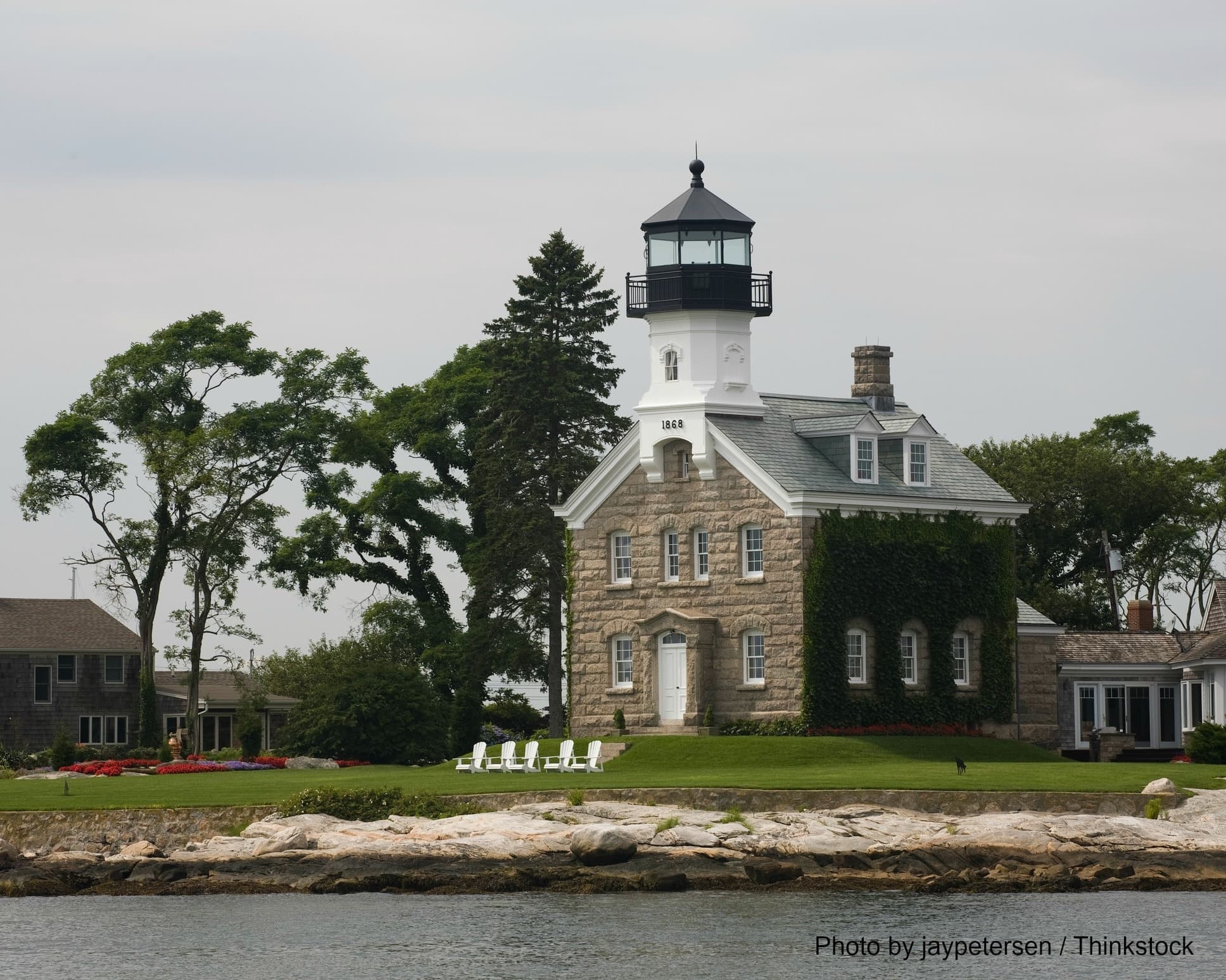A picturesque lighthouse with a stone facade surrounded by greenery and water.