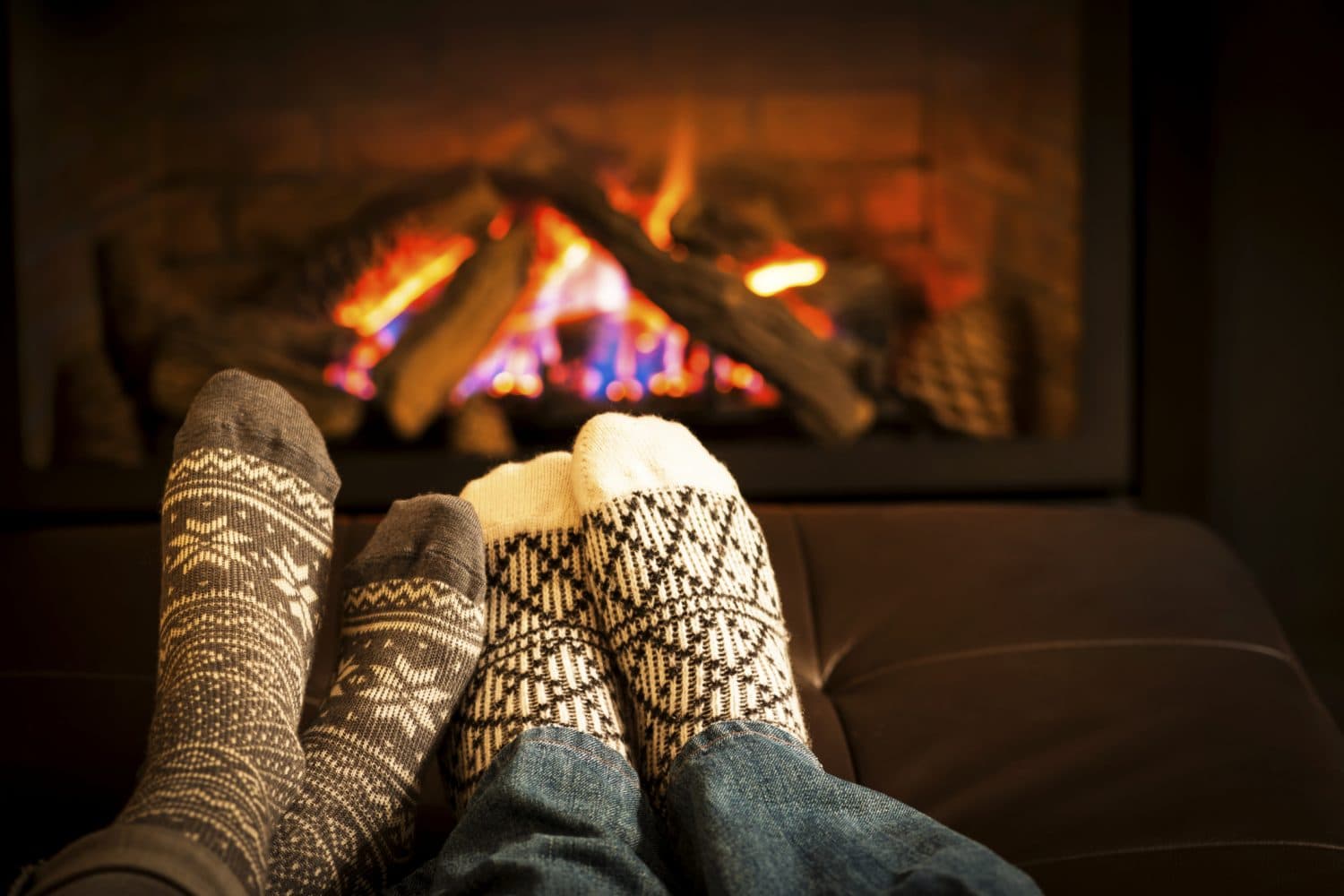 Two pairs of cozy, patterned socks resting on a couch in front of a warm fireplace.