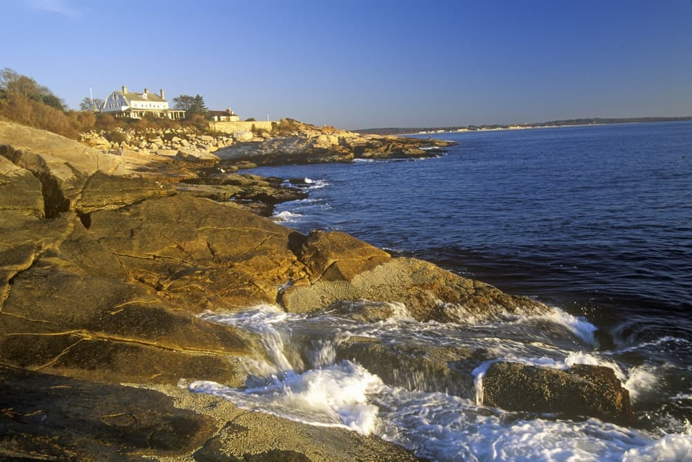 Coastal rocks lead to a calm ocean under a clear blue sky.