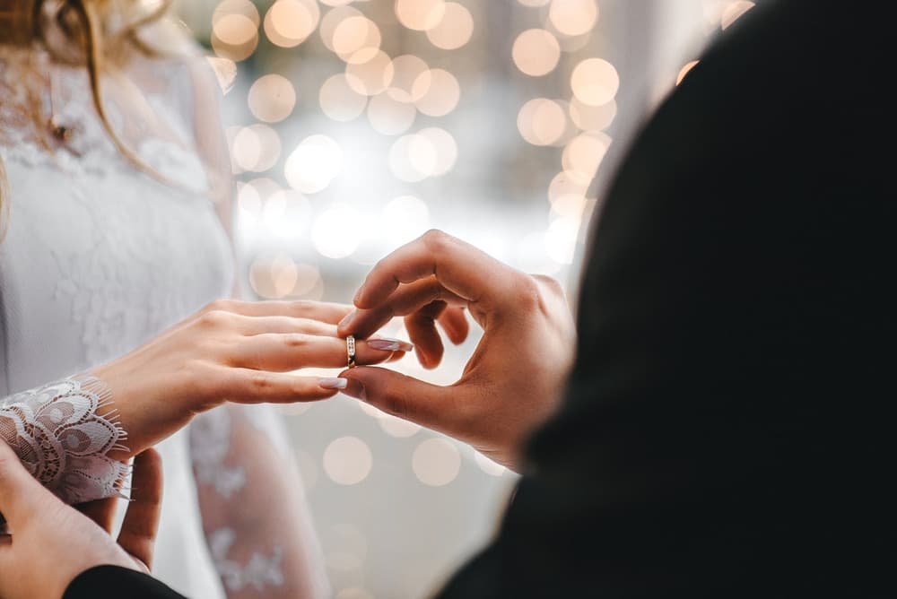 A couple exchanges wedding rings in a softly lit setting.