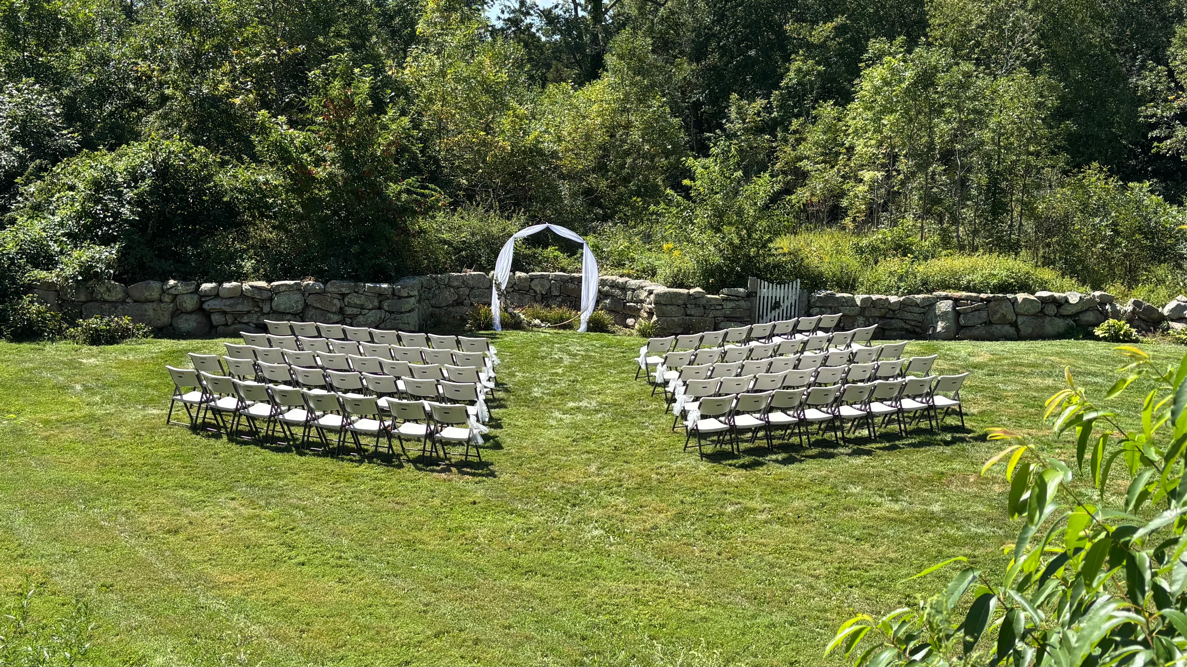 An outdoor wedding setup featuring rows of empty chairs arranged around a ceremonial arch.