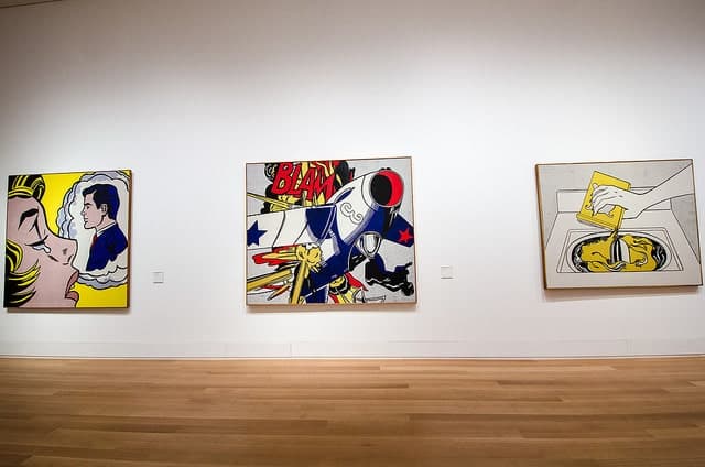 Three colorful pop art paintings are displayed on the white wall of an art gallery.